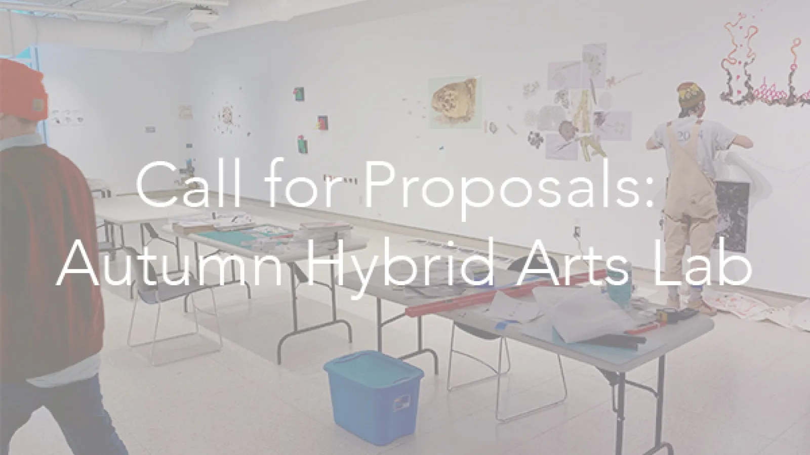 overview shot of two people in a gallery with a folding table between them, text overlay that says "call for proposals: autumn hybrid arts lab"