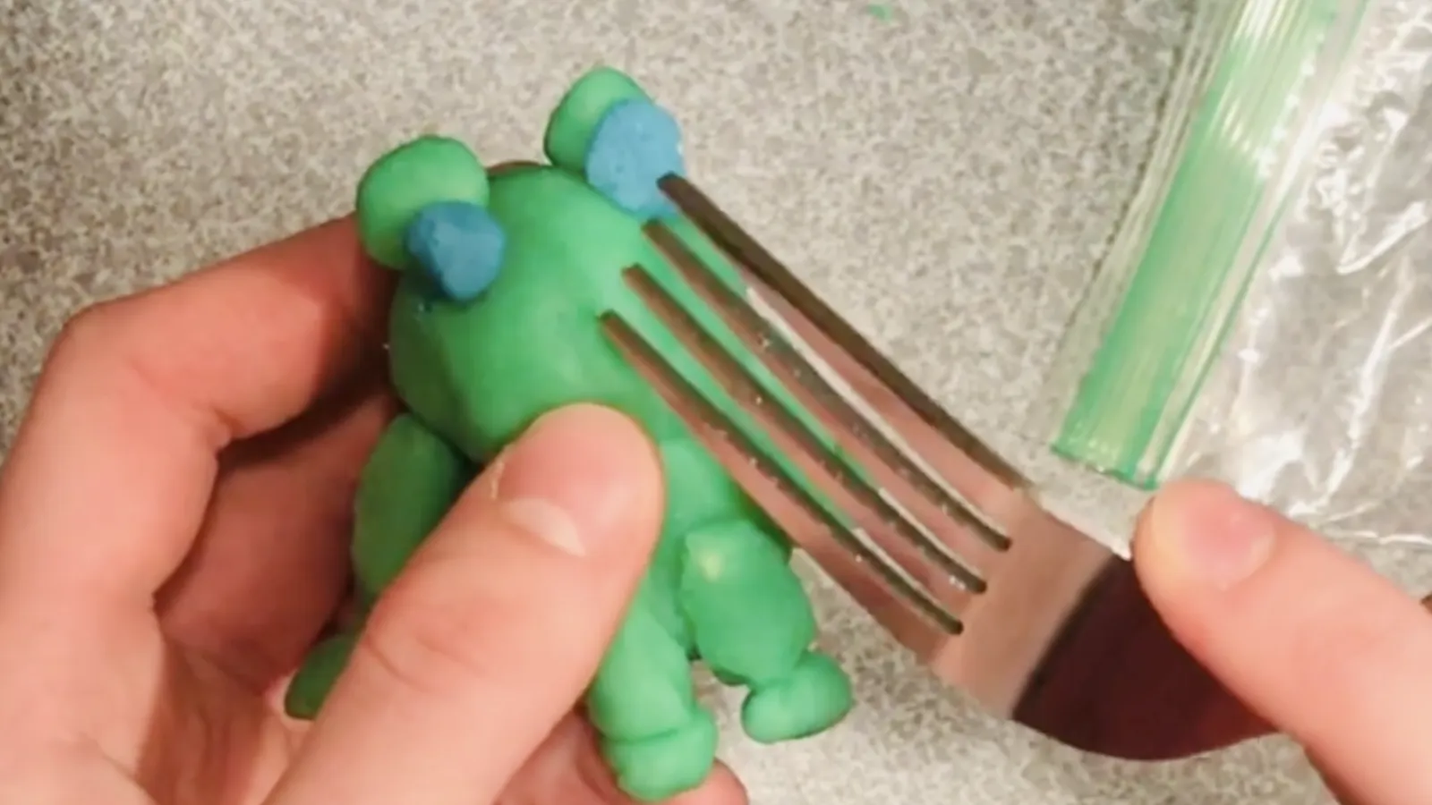 still from video, a clay frog is being held as a fork is used to create the imprint of a nose
