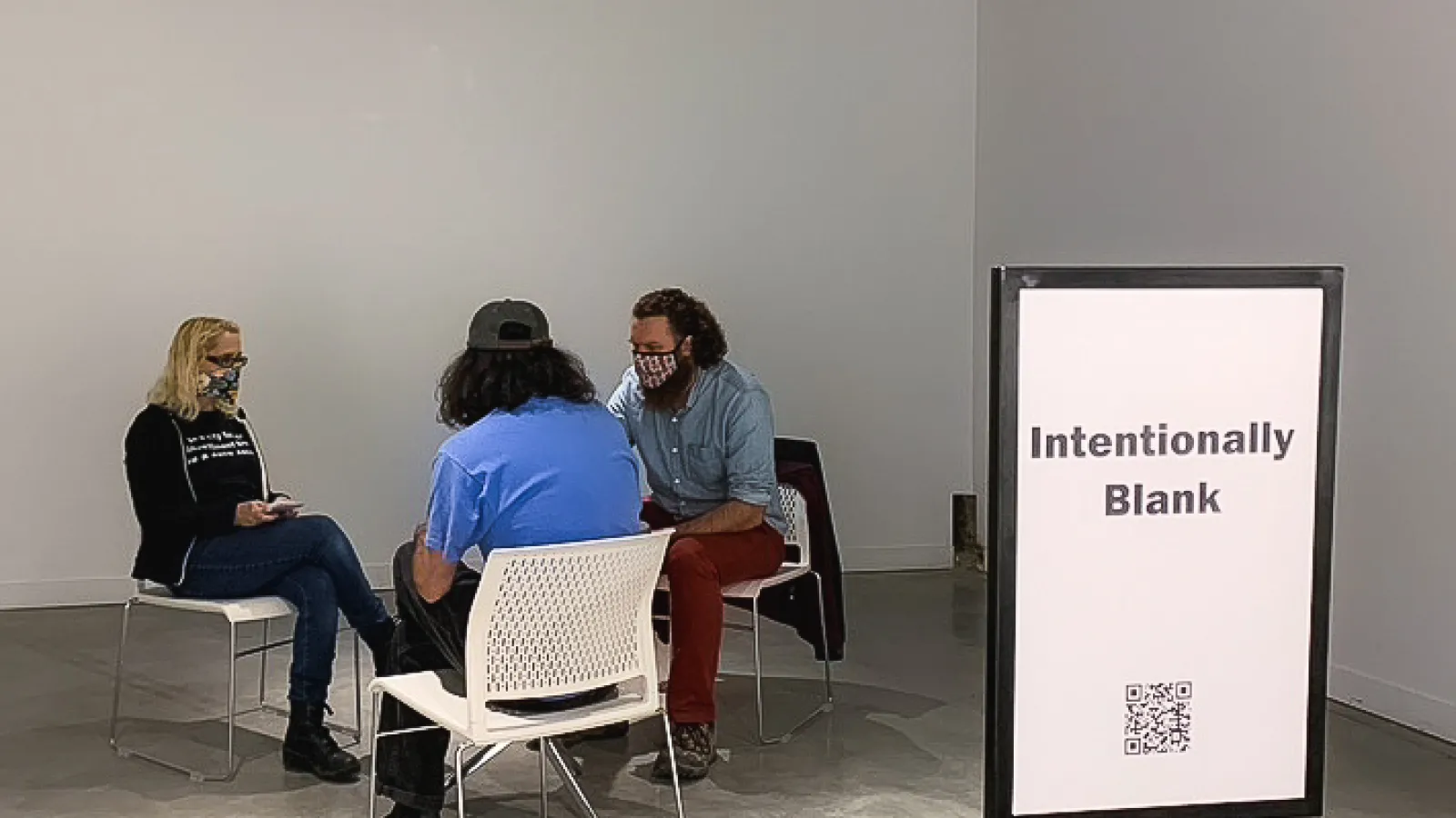 Three people sitting at a table. A sign in front of them says "Intentionally Blank" 