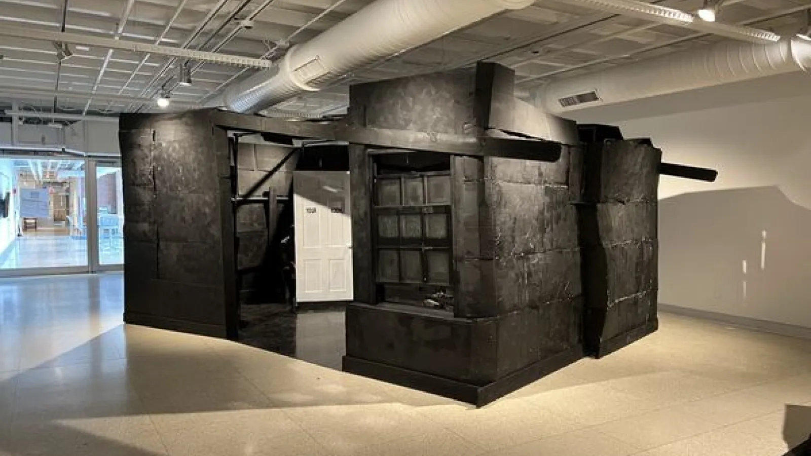 A fabricated house inside the gallery with black painted walls and a white door that says Your Room