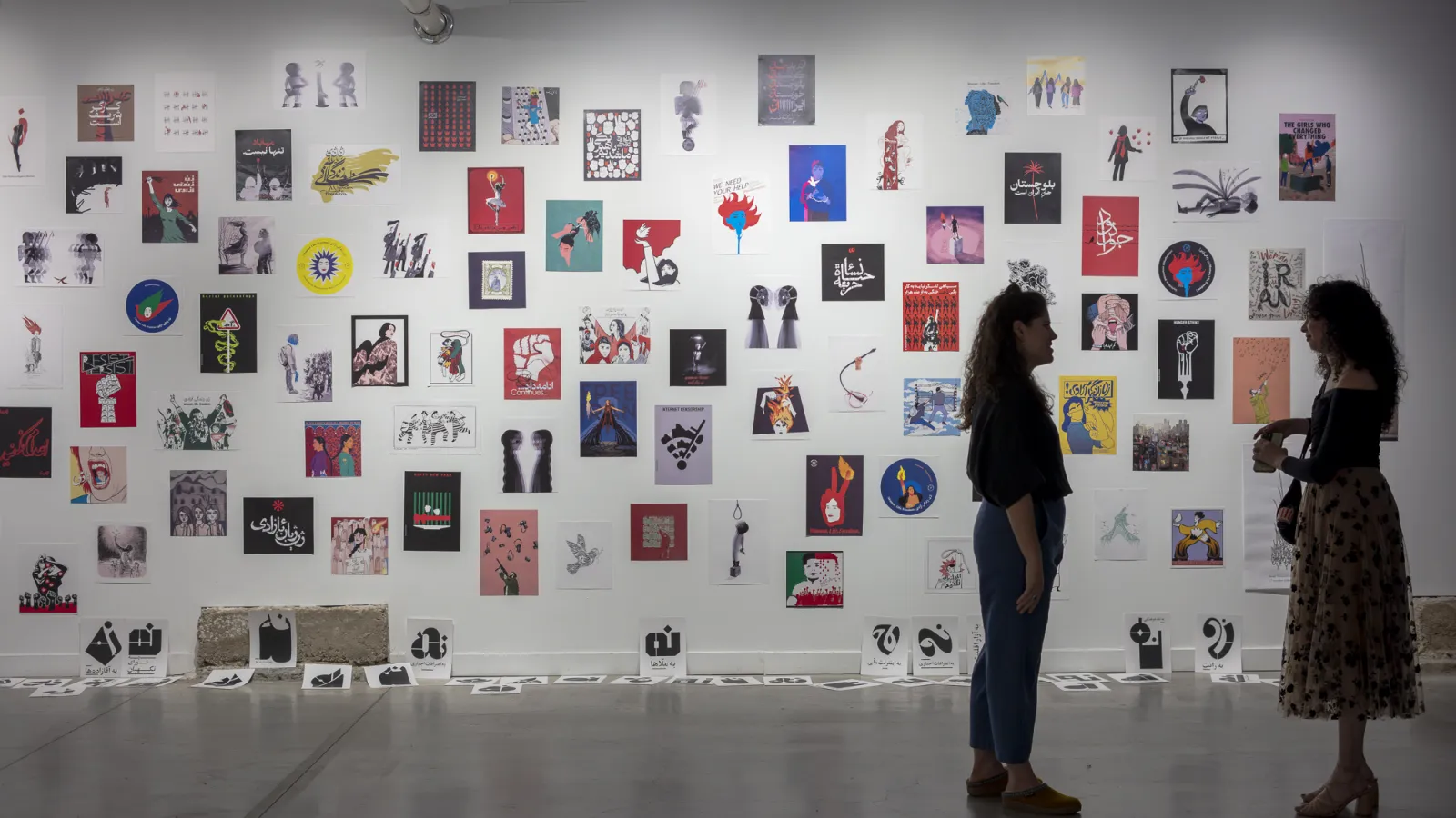 Two visitors in front of the wall of the traveling poster show by Iranian artists