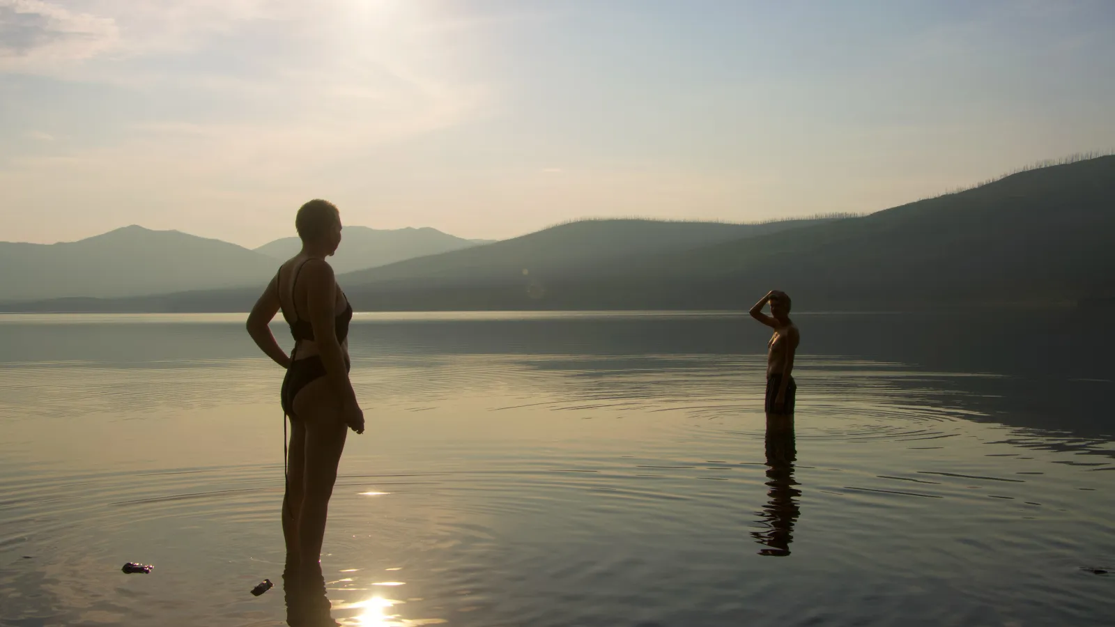 Two people standing in water with the sun reflecting, mountains in the distance