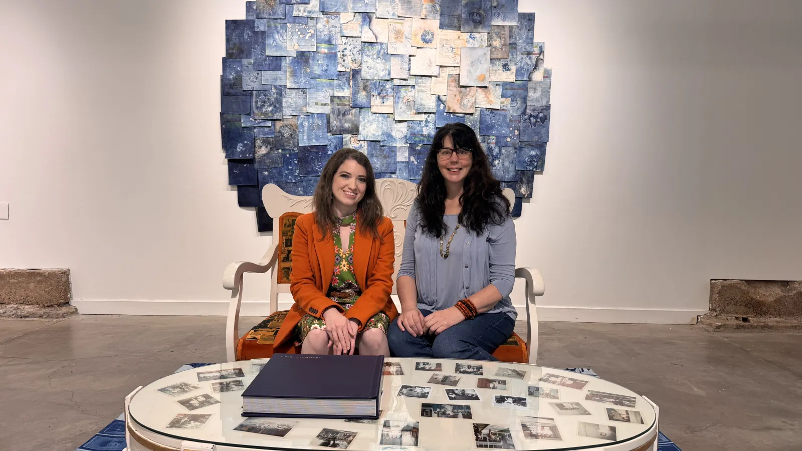 Diane Callahan (left) in an orange jacket and Michelle Burdine (right) in a blue shirt in front of a round blue cyanotype collage