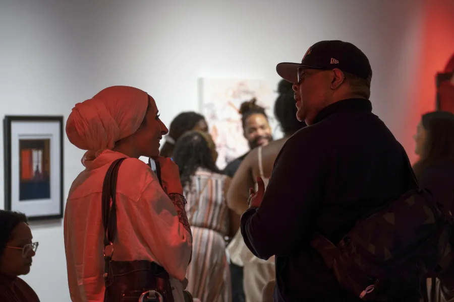 Two individuals speaking to each other in front of a gallery lit in red
