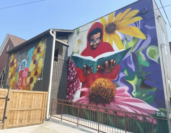 A mural of an african american man in a red hoodie holding a book in front of a purple background with sunflowers