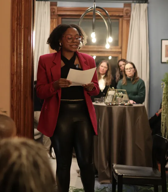a woman of color in a red pants suit standing in a door way and holding a paper with observers behind her