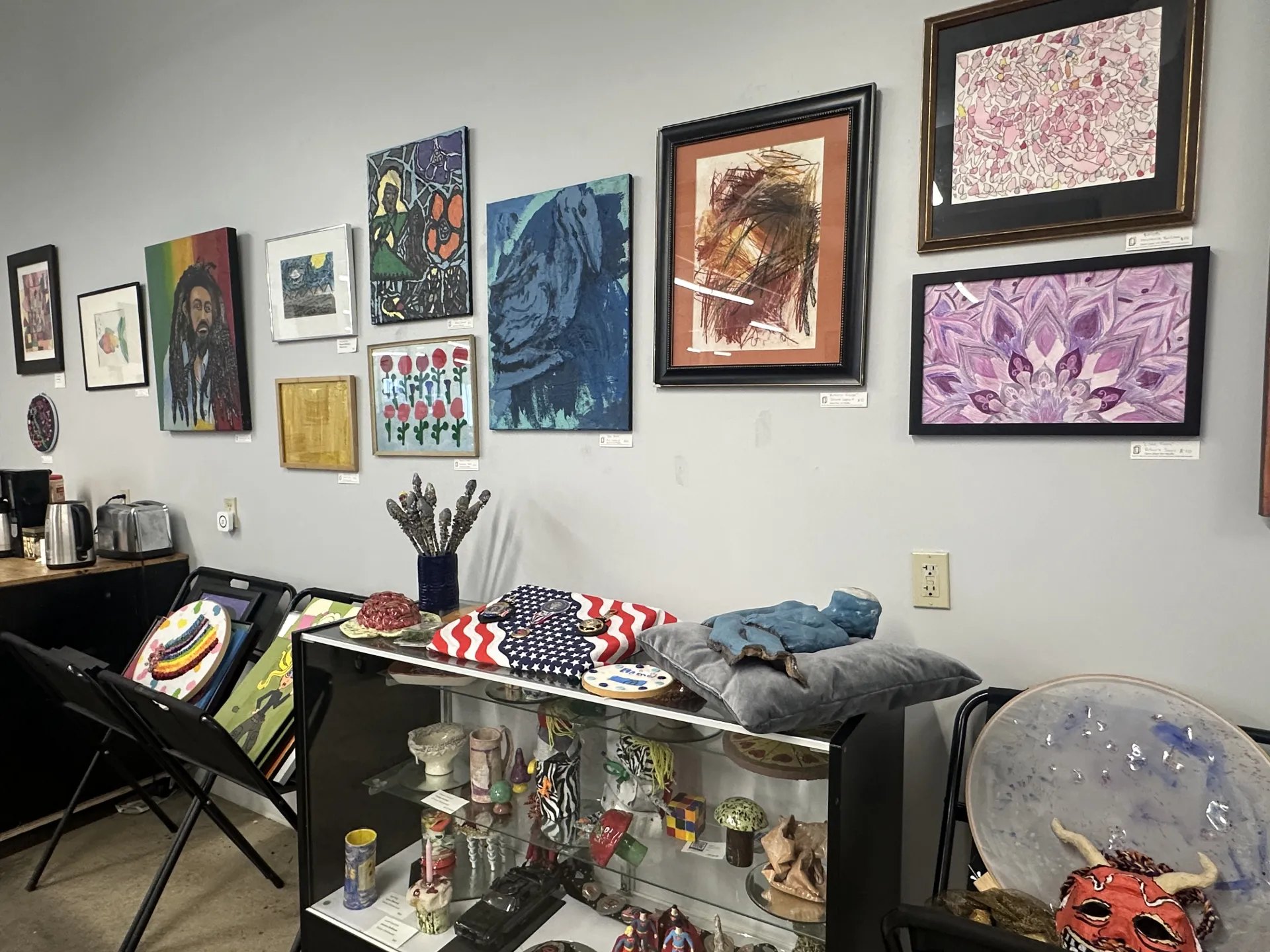 wall with many framed paintings and a shelf of various small sculptures