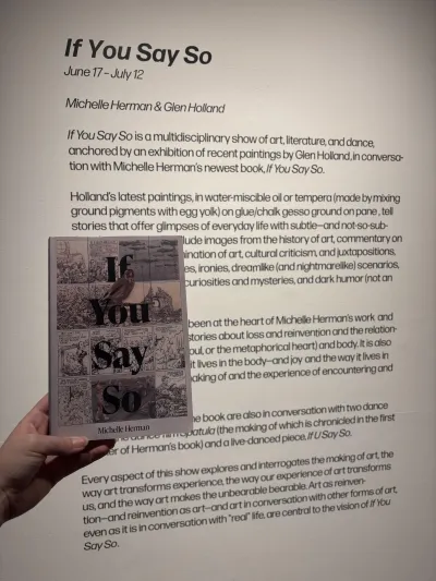 If You Say So book being held in front of an exhibition description for the If You Say So show